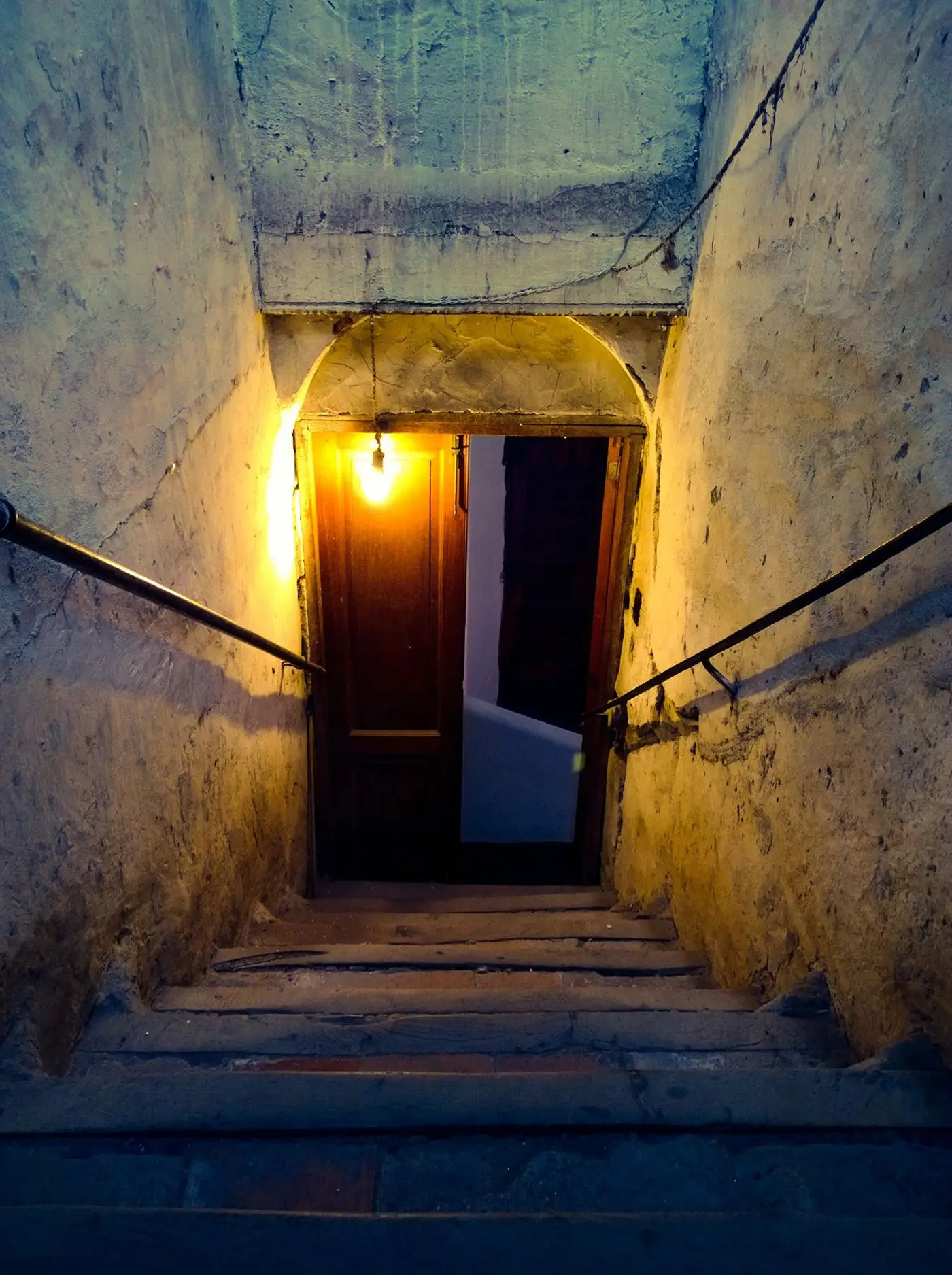 Steintreppe mit Glühbirne führt zu einer alten Kellertür