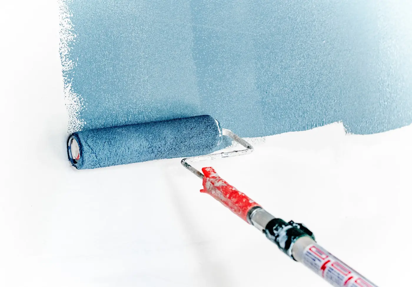 Farbroller trägt hellblaue Farbe auf eine weiße Wand auf