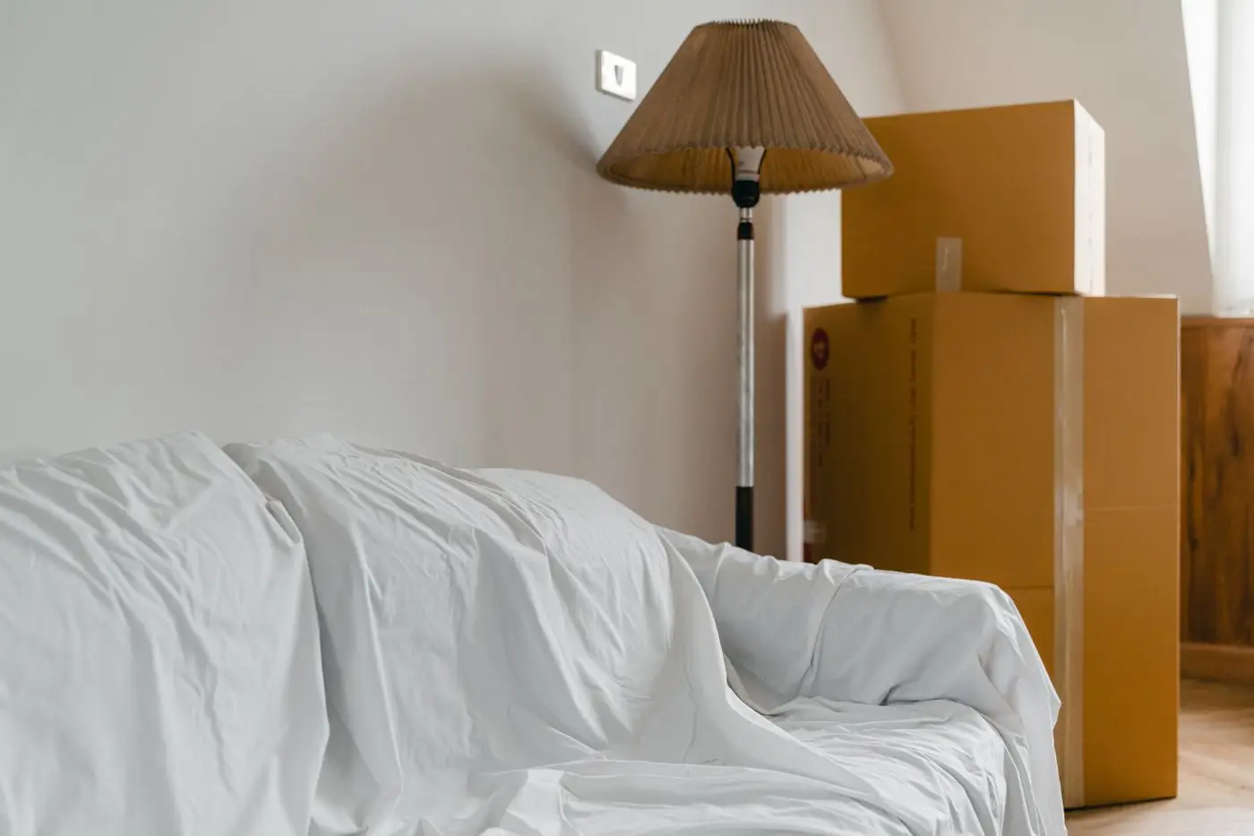 Abgedecktes Sofa, Stehlampe und gepackte Umzugskartons in einer Wohnung